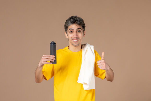 准备正面图：年轻男子拿着泡沫和毛巾准备在粉色背景上刮胡子泡沫脸毛巾