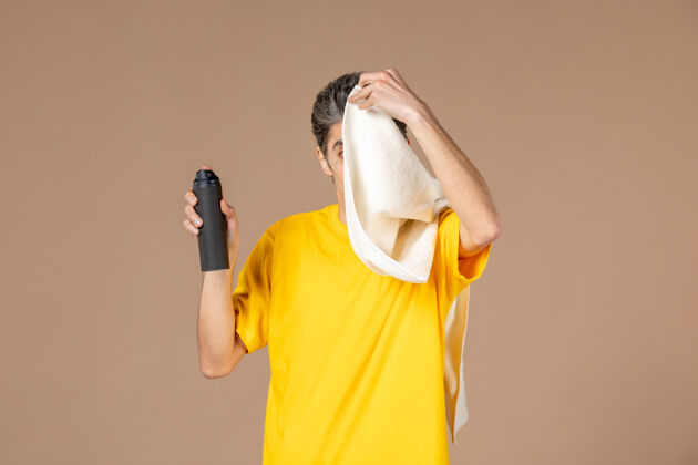 泡沫正面图：年轻男子拿着泡沫和毛巾准备在粉色背景上刮胡子视图准备男性