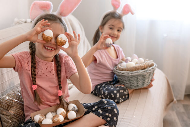 复活节有兔子耳朵的小姐妹们 家里的沙发上放着复活节彩蛋庆祝女孩节日