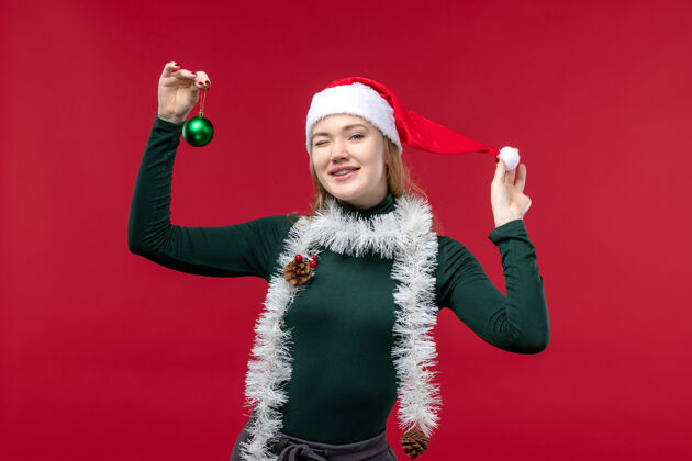 圣诞节正面图红色背景上手持玩具的年轻女性 戴着花环红色成人人物
