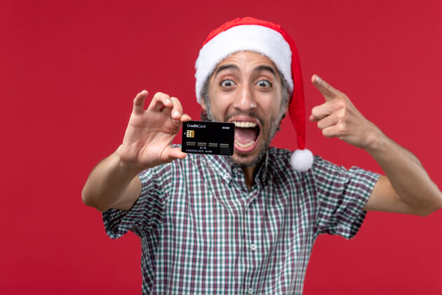 圣诞节正面图：年轻男性在红色背景下展示银行卡男性红色年轻男性