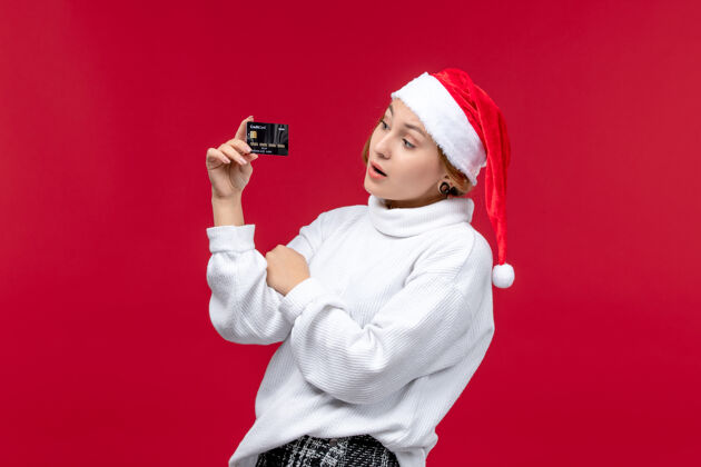 幼儿正面图年轻女子拿着银行卡在红地板上圣诞假期红钱卡片前面人