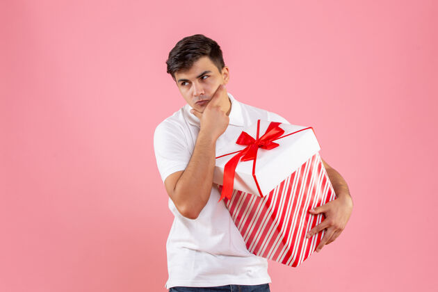 思考正面图：年轻男性 带着大大的圣诞礼物 在粉色背景上思考礼物年轻男性肖像