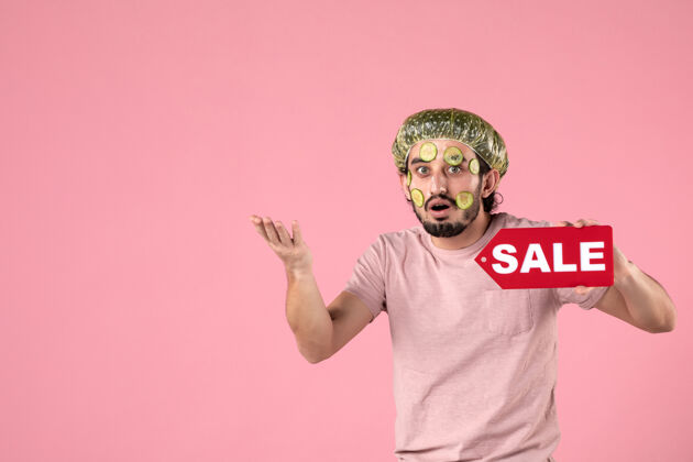 肖像正面图：年轻男性 脸上戴着面具 手持粉色背景的销售铭牌自我照顾视图顺利