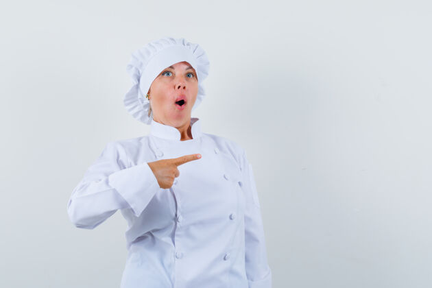 脸穿着白色制服的女厨师指着一边 看上去很惊讶时尚惊讶自信