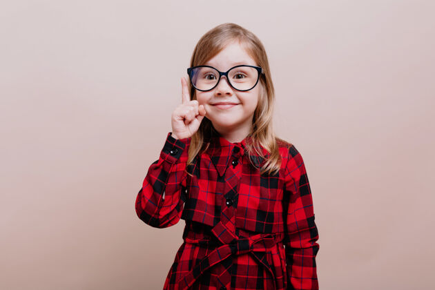 眼睛滑稽聪明的小女孩的画像戴着眼镜和格子衬衫抬起一个手指和微笑在前面快乐年轻可爱