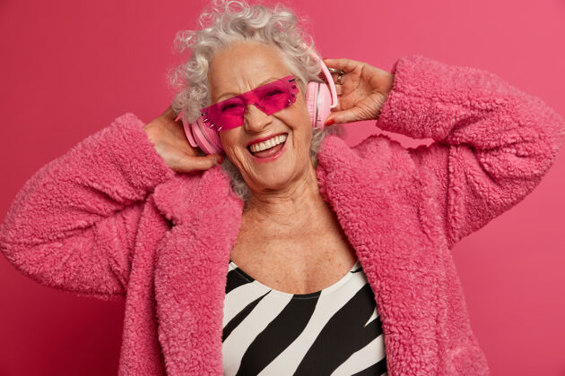 放松穿着粉色紧身衣和外套 满脸皱纹的时尚老奶奶的特写照片音乐肖像快乐