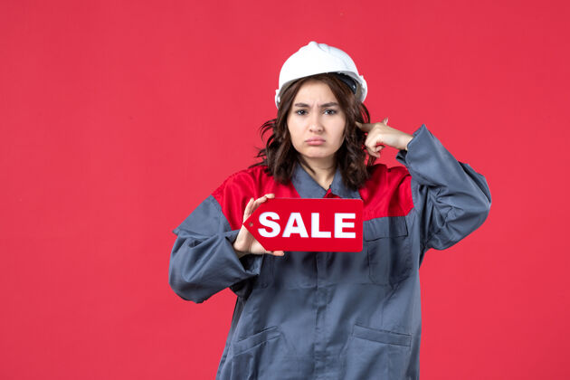 穿正面是穿着制服 戴着安全帽 孤零零的红墙上展示销售图标的女员工的近景景点女工微笑