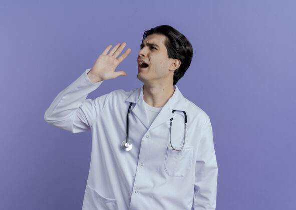长袍年轻的男医生穿着医用长袍 手持听诊器 头转向一边 手靠近嘴巴 对着隔离在紫色墙壁上的人大声喊叫 还有复印空间保持穿手