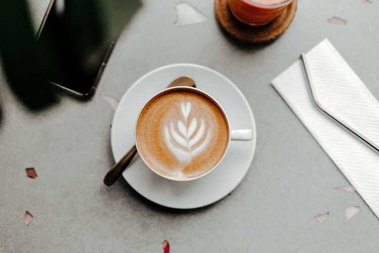 自然咖啡杯顶视图 泡沫和奶油 餐巾上的塑料吸管和大理石灯桌上的电话咖啡厅表面