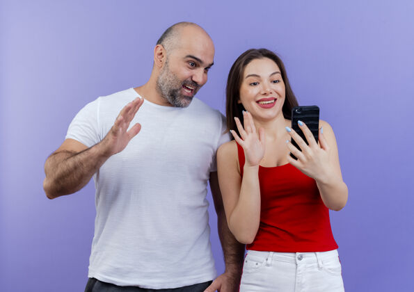 女人一对微笑的成年夫妇拿着手机的女人给男人留下了深刻的印象 男人一边看着手机一边挥手挥手成人印象