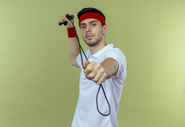 运动戴着头巾的年轻运动型男子拿着跳绳 用食指指着相机 看上去自信满满年轻跳过看