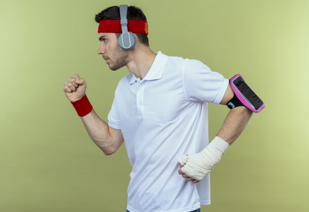 手臂戴着头戴式耳机和智能手机臂带的年轻运动型男子在绿茵场上努力训练运动耳机努力