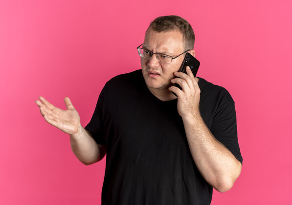 超重戴眼镜的超重男子身穿黑色t恤 一边用粉色手机交谈 一边显得困惑和不快而穿男士