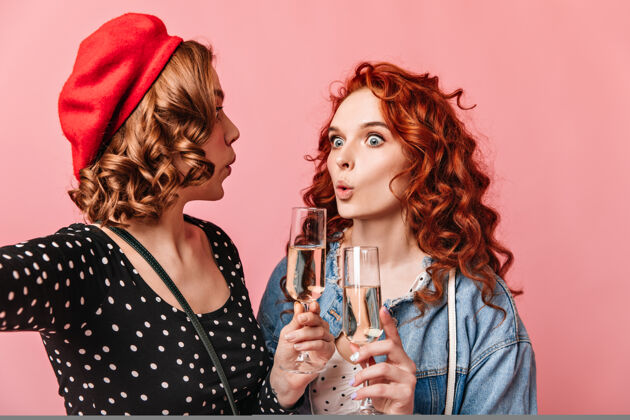 漂亮惊讶的女士们喝香槟摄影棚拍摄的惊讶的女孩拿着粉红色背景的酒杯祝酒饮料年轻人