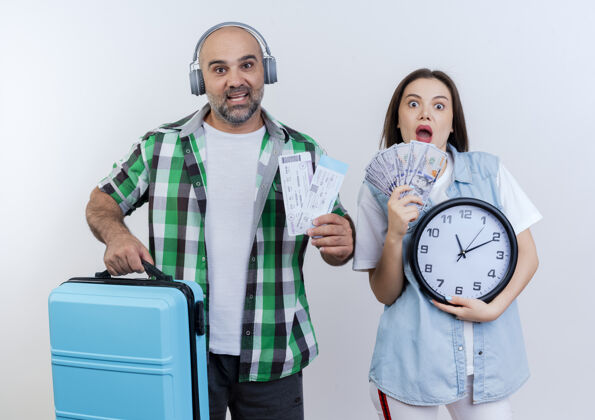 女人印象深刻的成人旅行者夫妇戴着耳机的男人拿着旅行票和手提箱的女人拿着钱和时钟都在看手提箱耳机男人