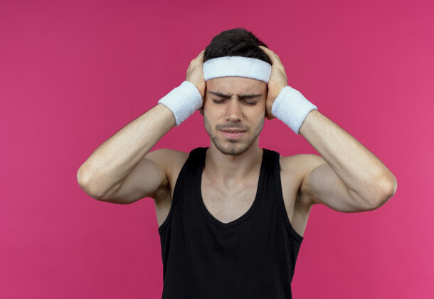 不适戴着头巾的年轻运动型男子看起来身体不适 双手抱着头 因粉红色而头痛得厉害头手运动