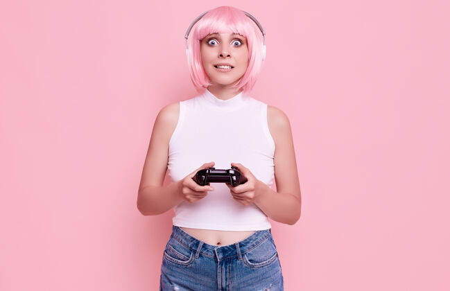 积极美丽快乐的游戏女孩与粉红色头发的肖像玩游戏机上五颜六色的操纵杆在工作室成人操纵杆玩家