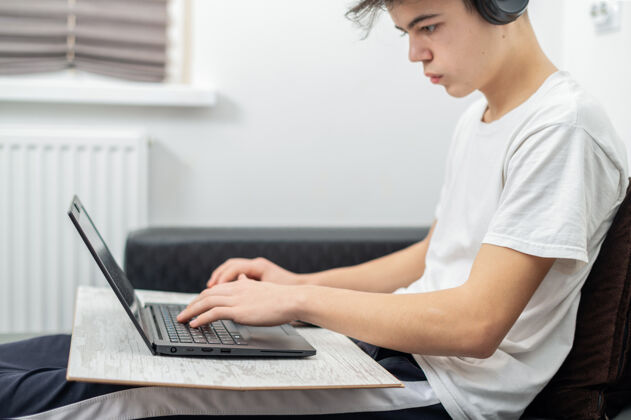 学校十几岁的男孩正在家里用带耳机的笔记本电脑严肃而专注的脸媒体儿童观看