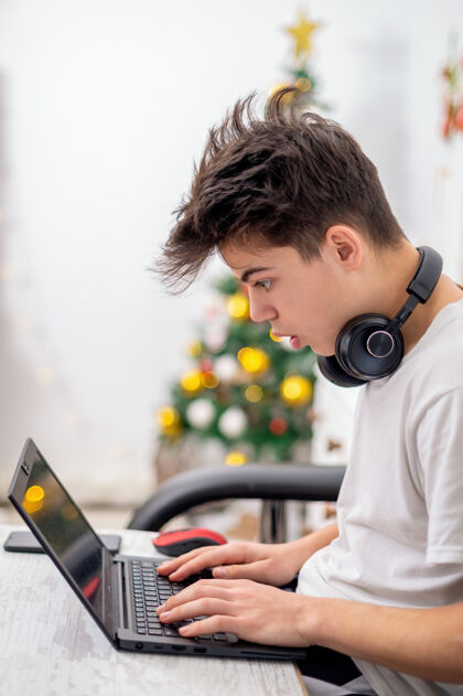 电话十几岁的男孩正在家里用带耳机的笔记本电脑圣诞树挂在墙上惊讶的脸长度便携播放器