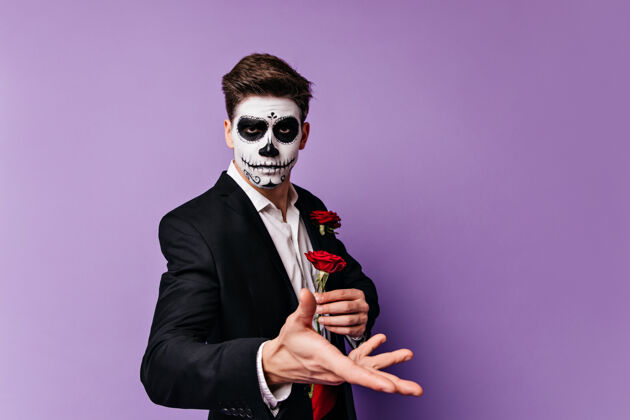 男人一个漂亮的年轻人 他手拿红玫瑰 在孤立的背景下摆出一副骷髅头像的样子室内死亡之日墨西哥