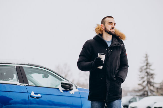 旅行穿着暖和夹克的帅哥站在被雪覆盖的汽车旁喝着咖啡季节人思考