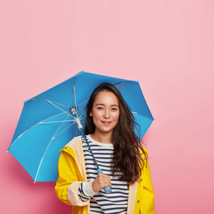 天快乐的黑头发东方女士 自然美丽 感觉干燥和保护 穿着防水雨衣 携带雨伞 享受自由时间在雨天秋天亚洲外套季节