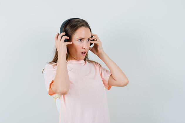 积极穿着粉色t恤 戴着耳机欣赏音乐的年轻女孩 看上去很惊讶 正前方的景色快乐微笑小
