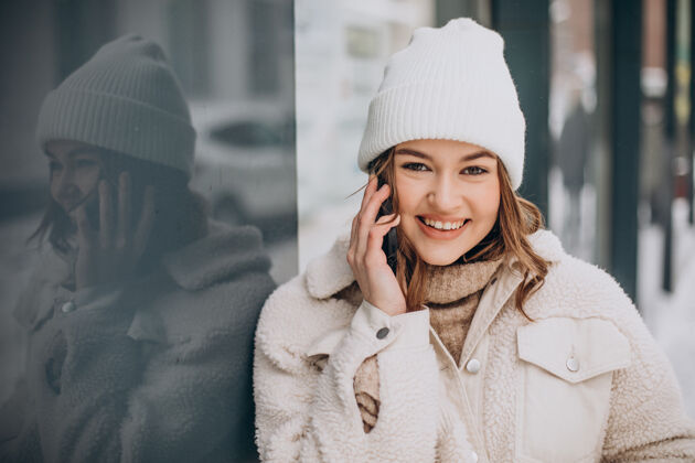 漂亮年轻女子在冬天的时候在街外用手机年轻毛衣女性