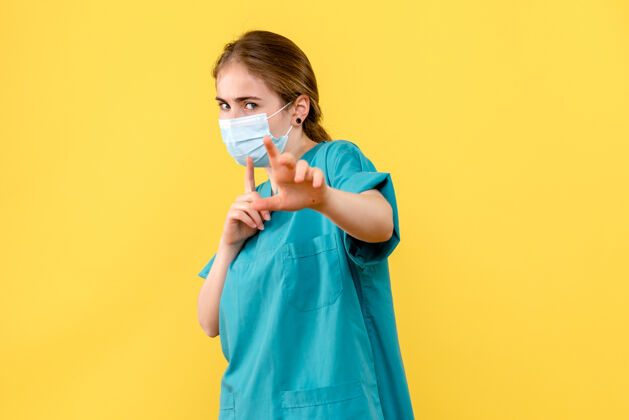脸正面图戴着面罩的女医生在一家黄色背景的卫生院大流行冠状病毒抱美女