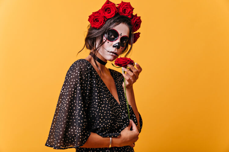 恐怖红色花冠上一头黑发的平静女孩的肖像戴着骷髅面具的女人享受着花香花传统年轻