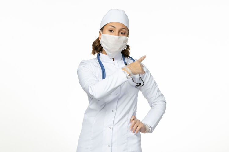 女性正面图女医生穿着白色医疗服 戴着口罩 因白墙上有冠状病毒大流行病毒病冠状病毒医学大流行人