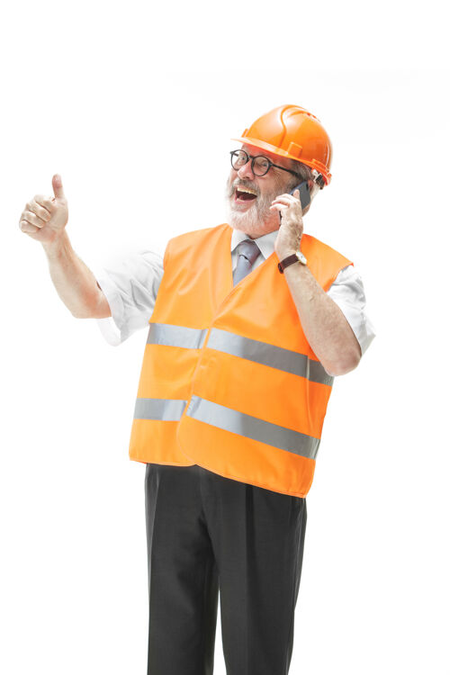 帽子一个穿着建筑背心 戴着橙色头盔的建筑工人在用手机谈论着什么设备黄色计划