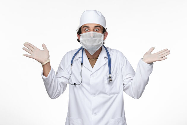 专业正面图身穿医疗服的男医生戴着口罩 以防白色办公桌上的病毒传染冠状病毒面罩病毒