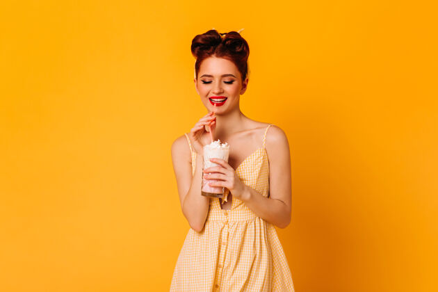 无忧无虑积极的红发女孩喝奶昔摄影棚拍摄的愉快的粉红色女士孤立在黄色空间表情饮料发型