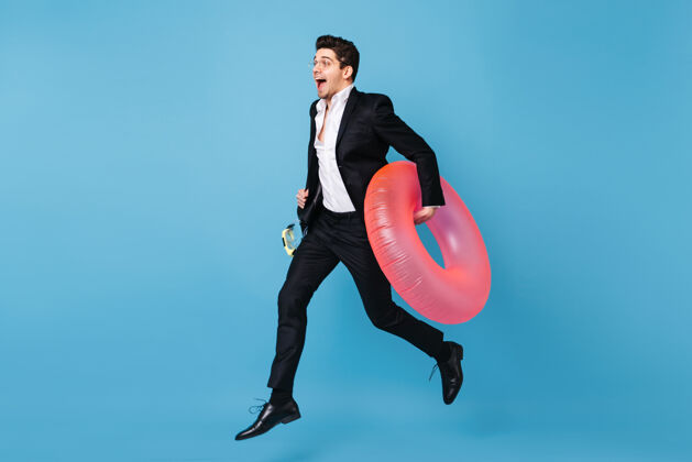 行政身着商务装的男子在蓝色空间奔跑的全长肖像 粉色充气圈搞笑经理员工