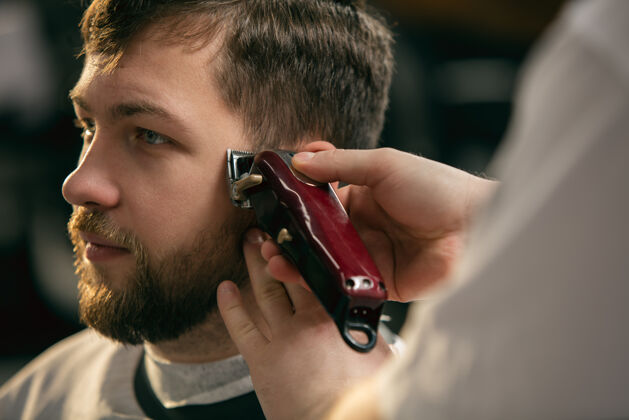 男性理发师 发型师的客户在得到护理和发型的新面貌理发店清洁剪刀