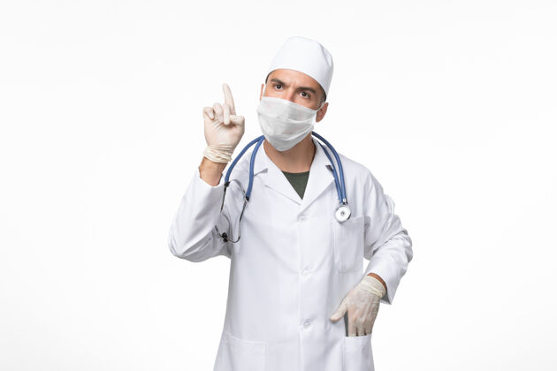 大流行正面图：男医生穿着医疗服 戴着防毒面具 在白色墙壁上抗击柯维德病大流行病毒男性视图男人