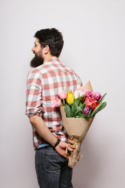 惊喜英俊的年轻人背着一束花 靠着白墙站着年轻时尚胡子