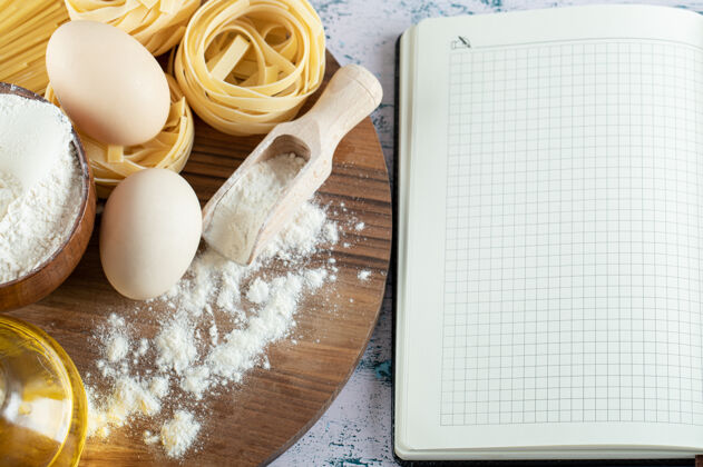生的在木板和笔记本上放油 鸡蛋和一碗面粉面食生的面粉