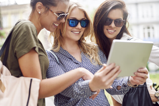 笑一群时尚女性在城市里享受和使用数码平板电脑触摸板抱着会议