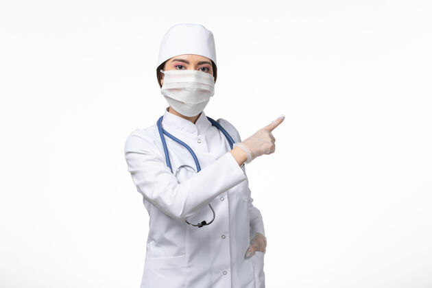专业正面图女医生穿着白色无菌医疗服 戴着口罩因冠状病毒-摆在淡白色墙壁上病毒冠状病毒-大流行性疾病面罩疾病正面