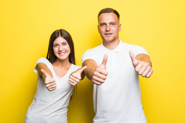 拥抱一对幸福的年轻夫妇竖起大拇指的肖像画被隔离在黄色上肖像男朋友成人