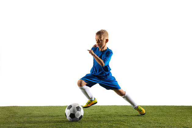 设备穿着运动服的足球运动员或足球运动员的小男孩 为了在白色场地上进球而用球假装或踢目标跑步活跃