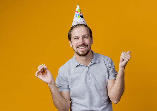站着戴着节日帽的年轻人站在橙色的墙上庆祝生日聚会快乐而兴奋地微笑着男人兴奋庆祝
