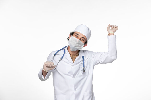 舞蹈正面图：男医生穿着医疗服 戴着面罩 以防在白墙上跳冠状病毒大流行飞溅面具西装
