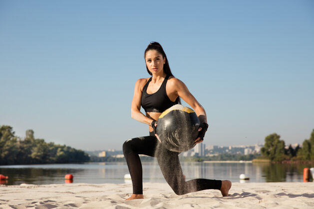 手臂年轻健康的女人在沙滩上带球做弓箭步日落健康沙滩