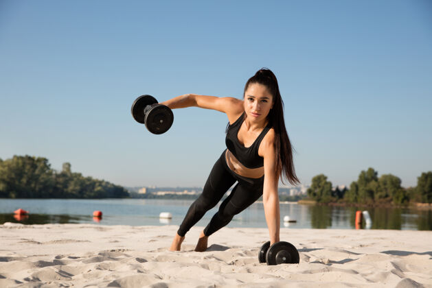 肌肉年轻健康的女子在沙滩上练习上身举重手臂强壮运动