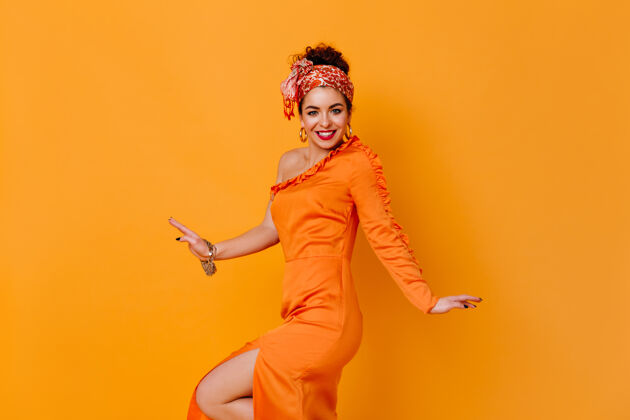姿势一位戴着不寻常头带 穿着开叉缎子连衣裙的女士在橙色的空间里微笑着长连衣裙现代完美