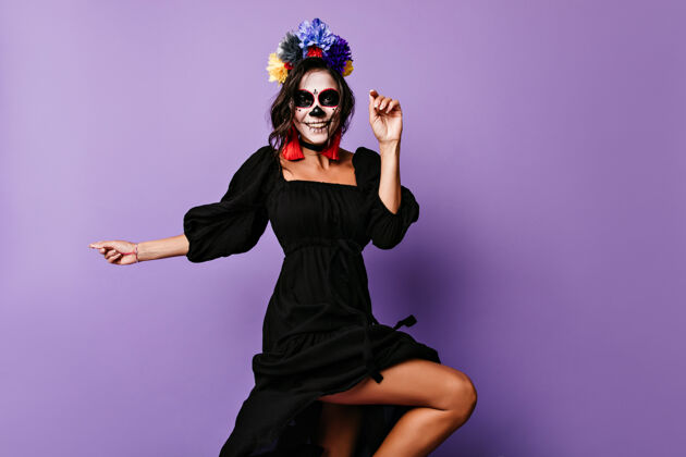 花身着黑色礼服的优雅笑脸女孩在死亡之日翩翩起舞身着僵尸妆的快乐拉丁女士庆祝万圣节女孩幽灵邪恶